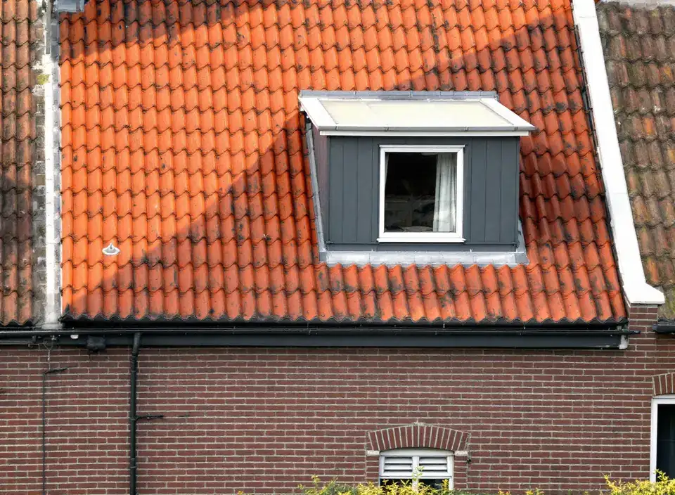 Een dakkapel met een plat dak en een donkere gevelbekleding midden in een oranje pannendak, met rijen pannen eronder en aan beide kanten